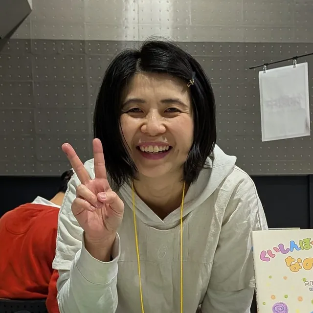 イベント会場で、絵本を並べたテーブルの前で笑顔でピースをするNodoka